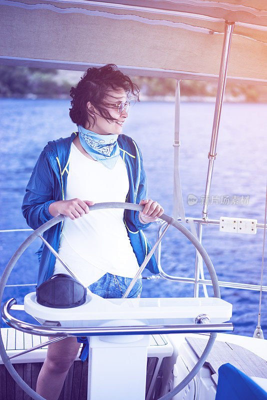 Woman standing behind the sailing wheel on a boat, sailing.